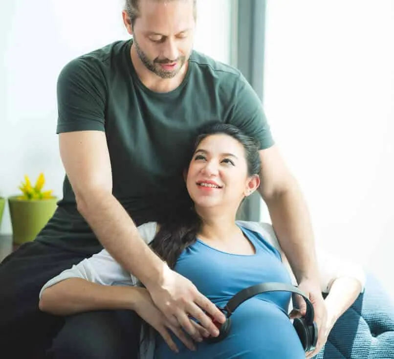 An expecting couple resting together, headphones on the belly